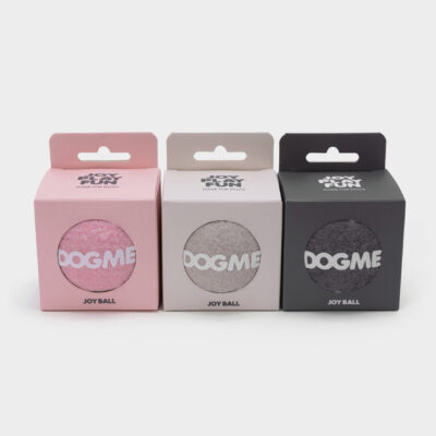 Três caixas Dogme Joy Ball nas cores rosa, cinza e preta com janela circular exibindo parte da bolinha texturizada